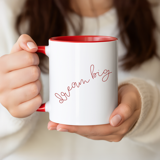 Person holding a white mug with red interior and handle, featuring the text 'Dream big' on a neutral background.