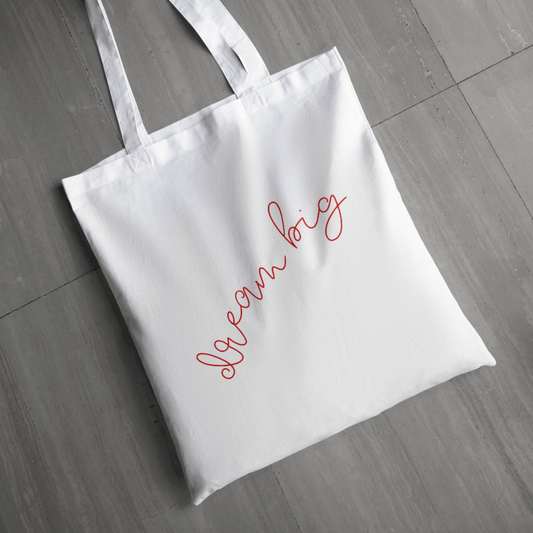 White tote bag with 'Dream Big' text on a wooden floor