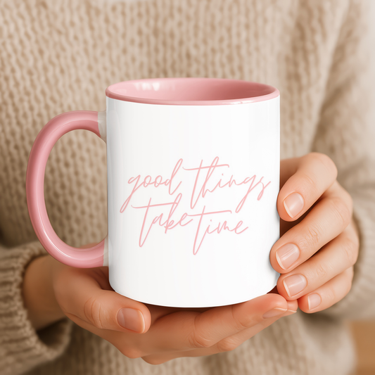 Person holding a white mug with pink interior and handle, featuring the text 'good things take time'.