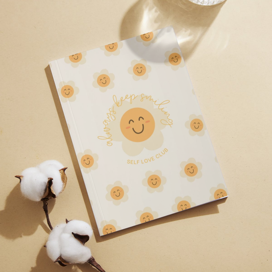 Notebook with flower and smiling face design on a beige background with cotton flowers.