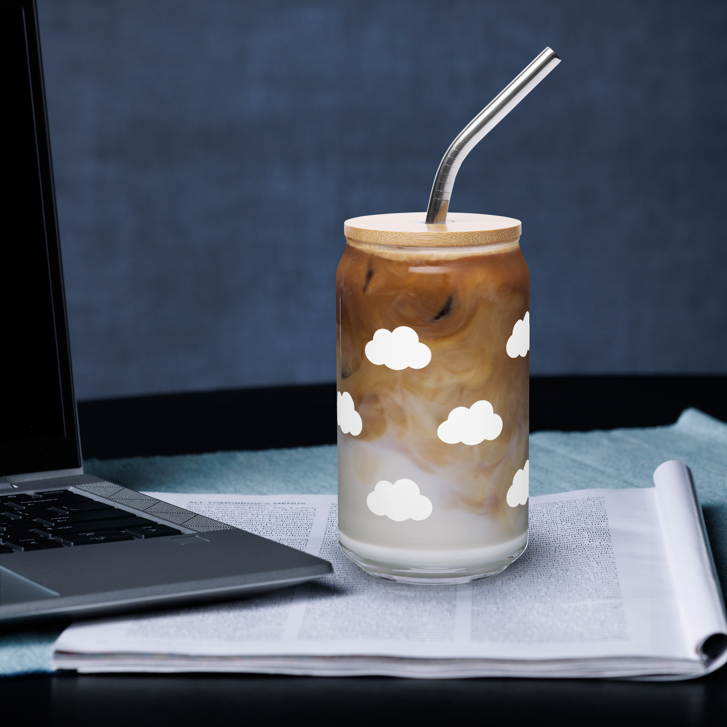 Glass of iced coffee with cloud patterns on a desk next to a laptop 