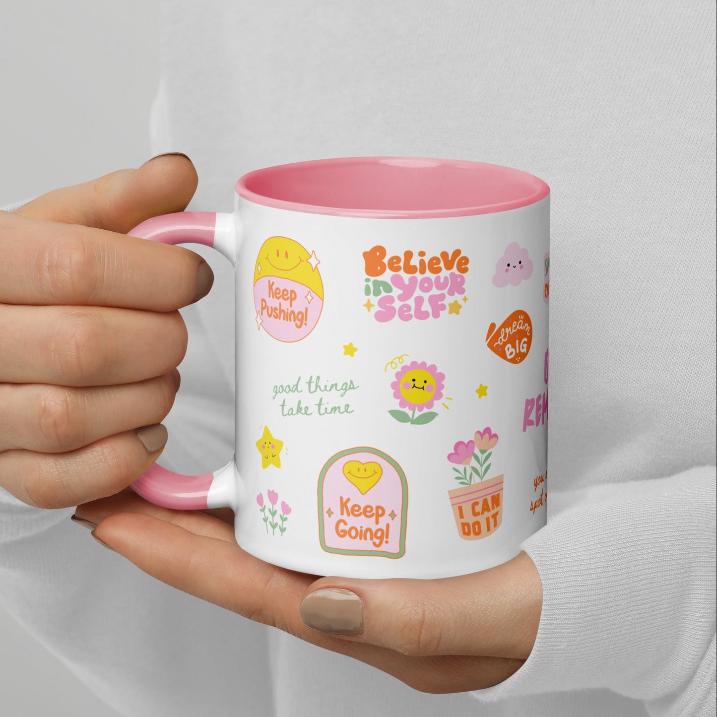 Person holding a mug with motivational phrases and designs on a plain background