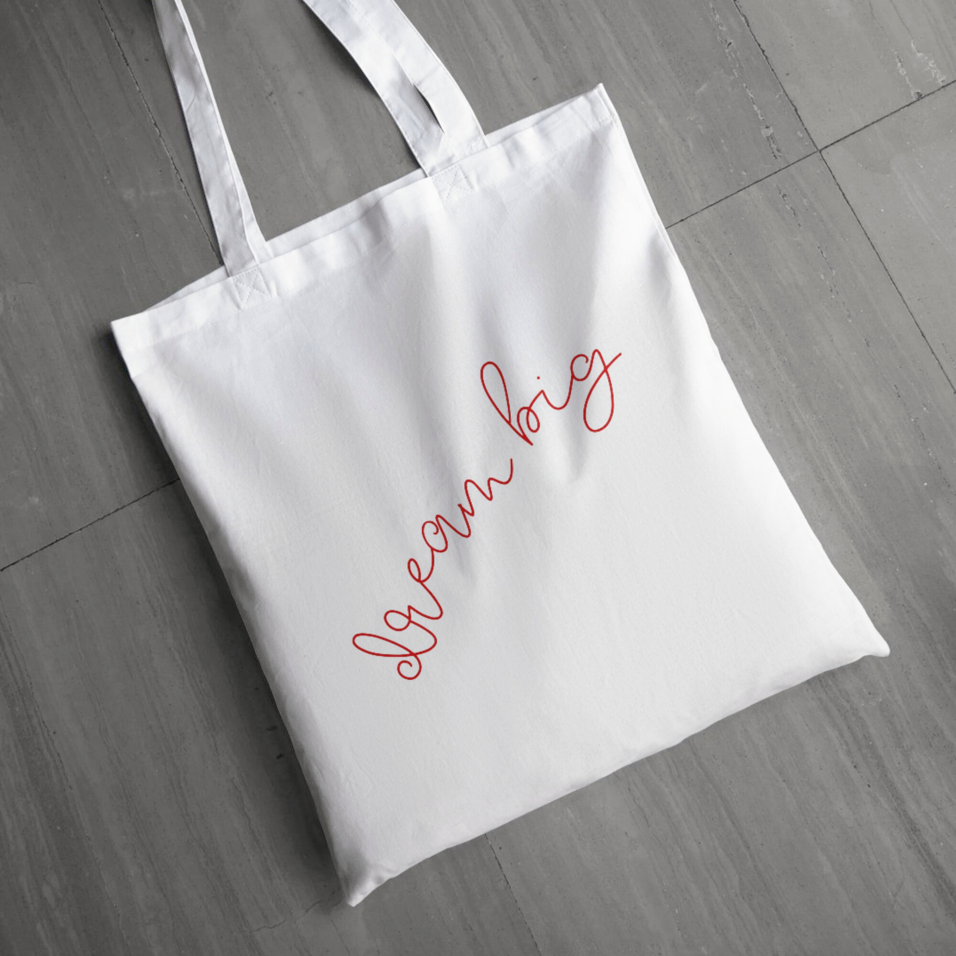 White tote bag with 'Dream Big' text on a wooden floor
