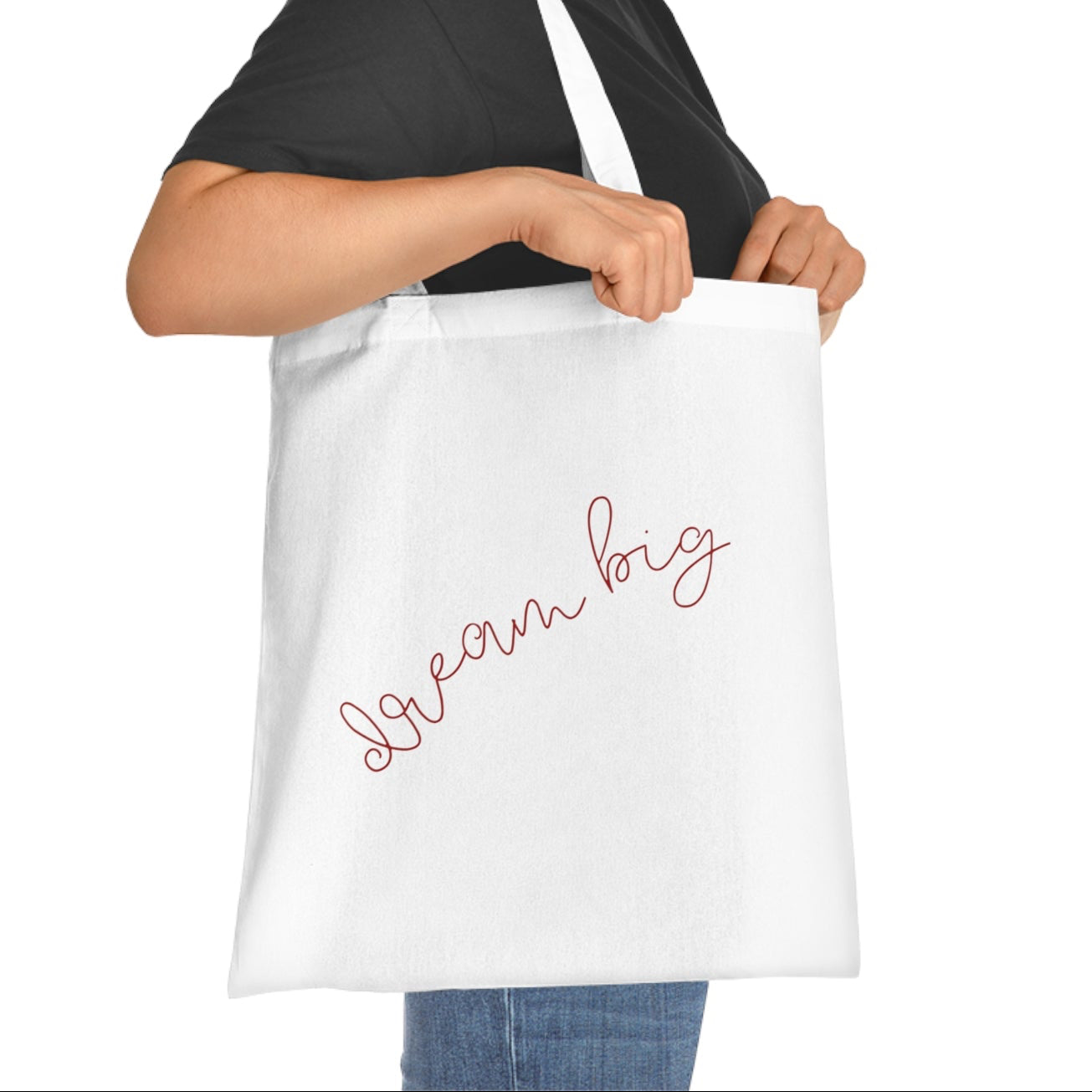 Woman holding a white tote bag with 'Dream Big' text on a white background