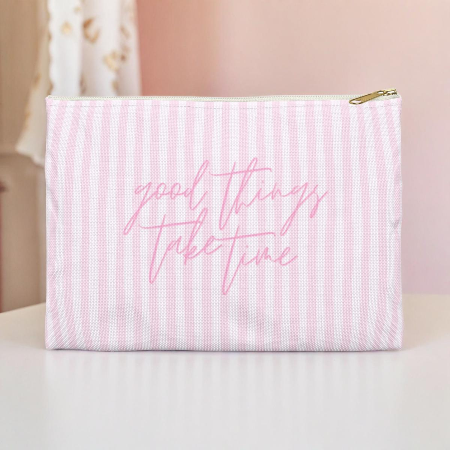 Pink striped pouch with 'good things take time' text on a light background