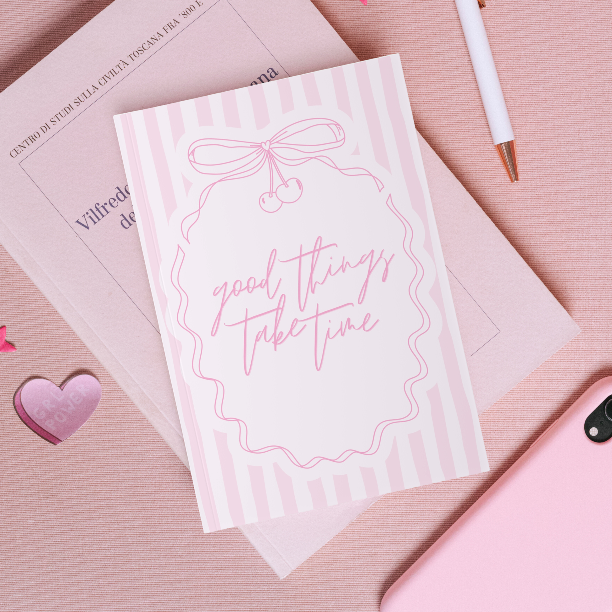Notebook with 'good things take time' text on a pink surface with a heart and pen.