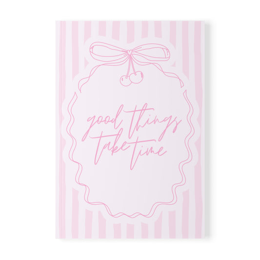 Notebook with 'good things take time' text and a bow design on pink striped background