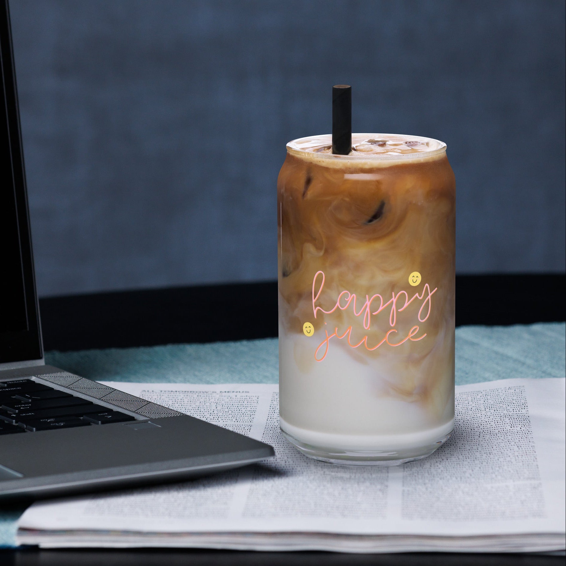 Iced coffee in a glass with 'happy juice' text next to a laptop on a desk.