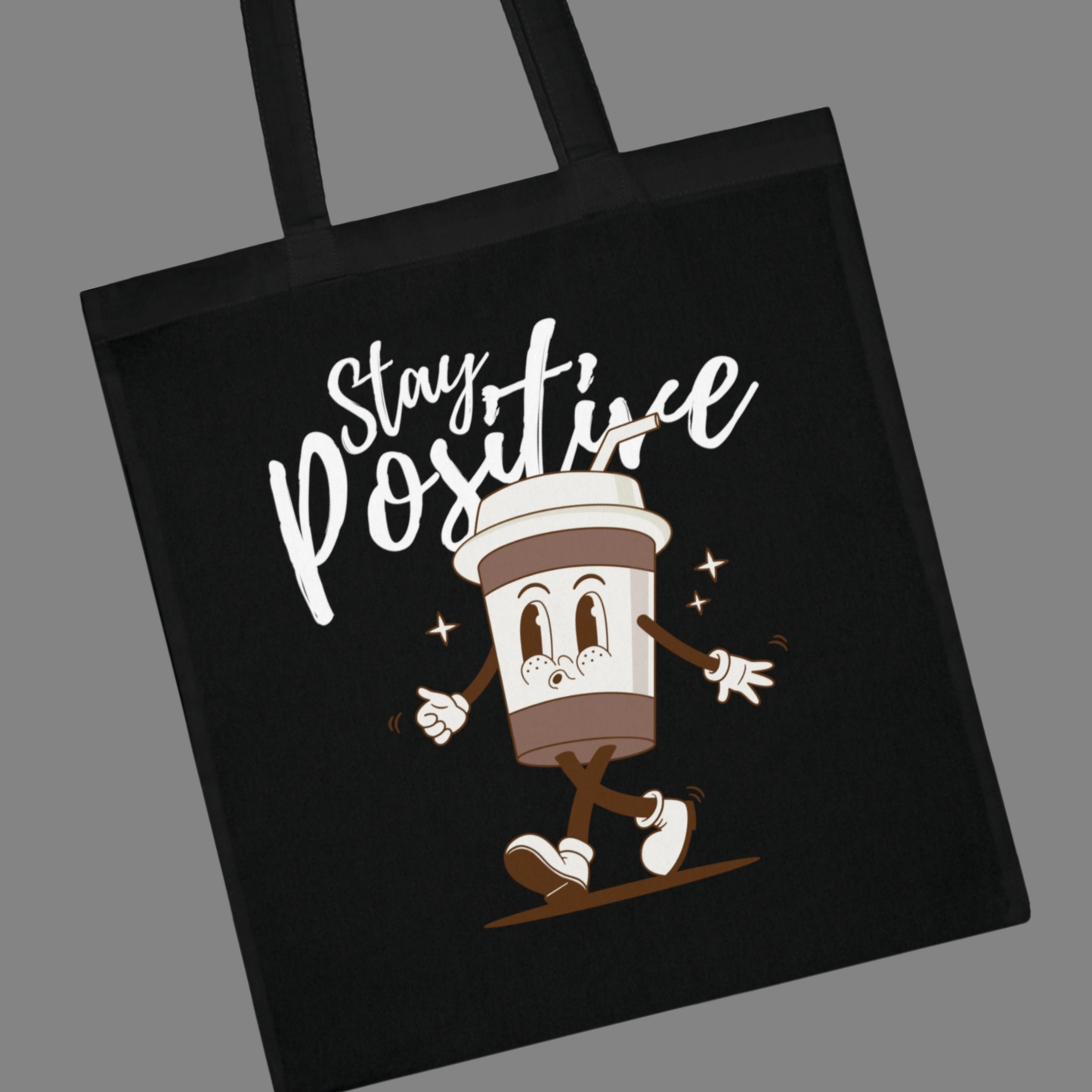 Black tote bag with a cartoon coffee cup character and 'Stay Positive' text on a gray background